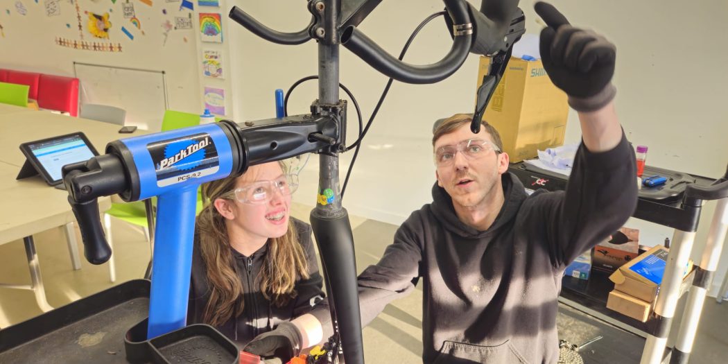 Connor offering training in his store, showing a young woman a bike in a stand