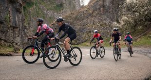A group of five cyclists on a road with a mountainous backdrop