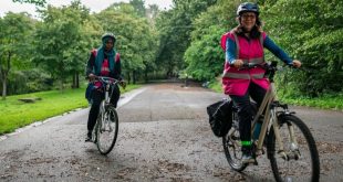 Two women cycling in pink vests in a park.